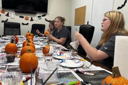 Religion students sit around a conference table painting pumpkins